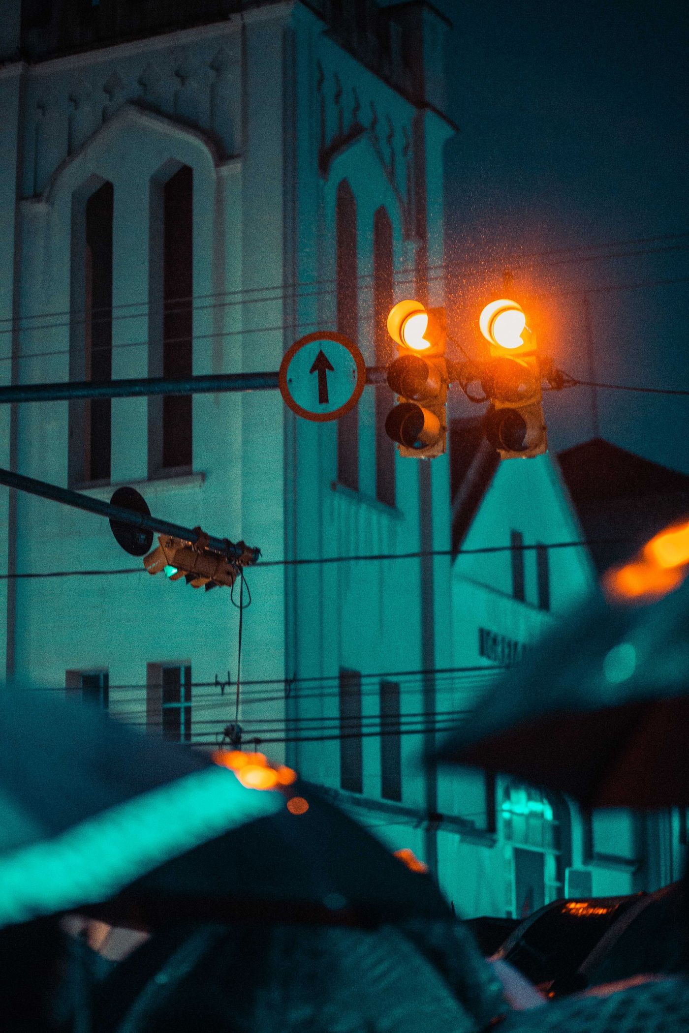 Amber traffic light against a teal wall at night